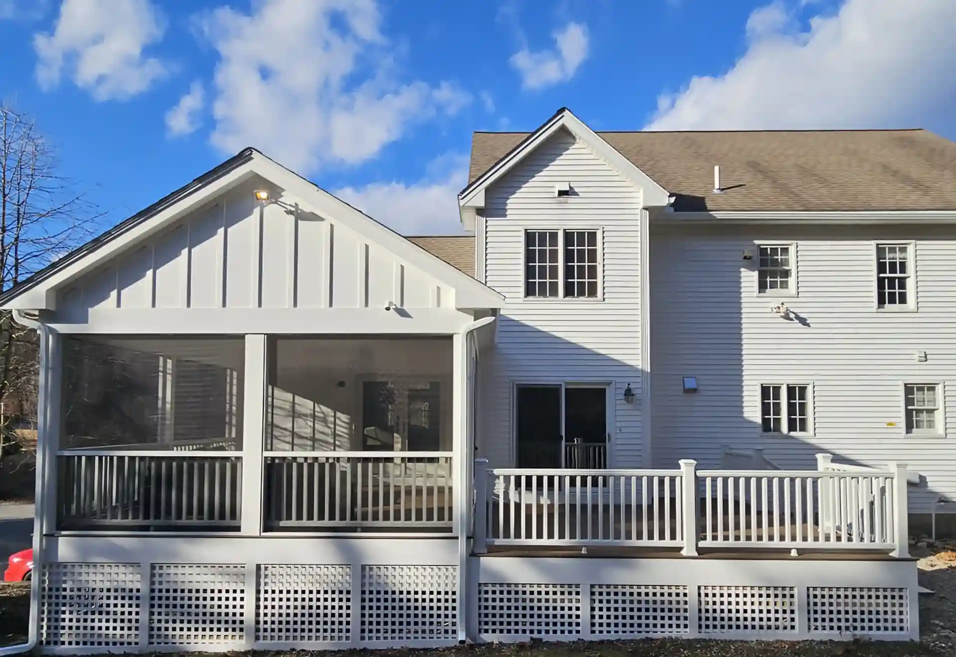 Rear view of house with screened porch and adjacent deck, white railing, and sliding glass door. 